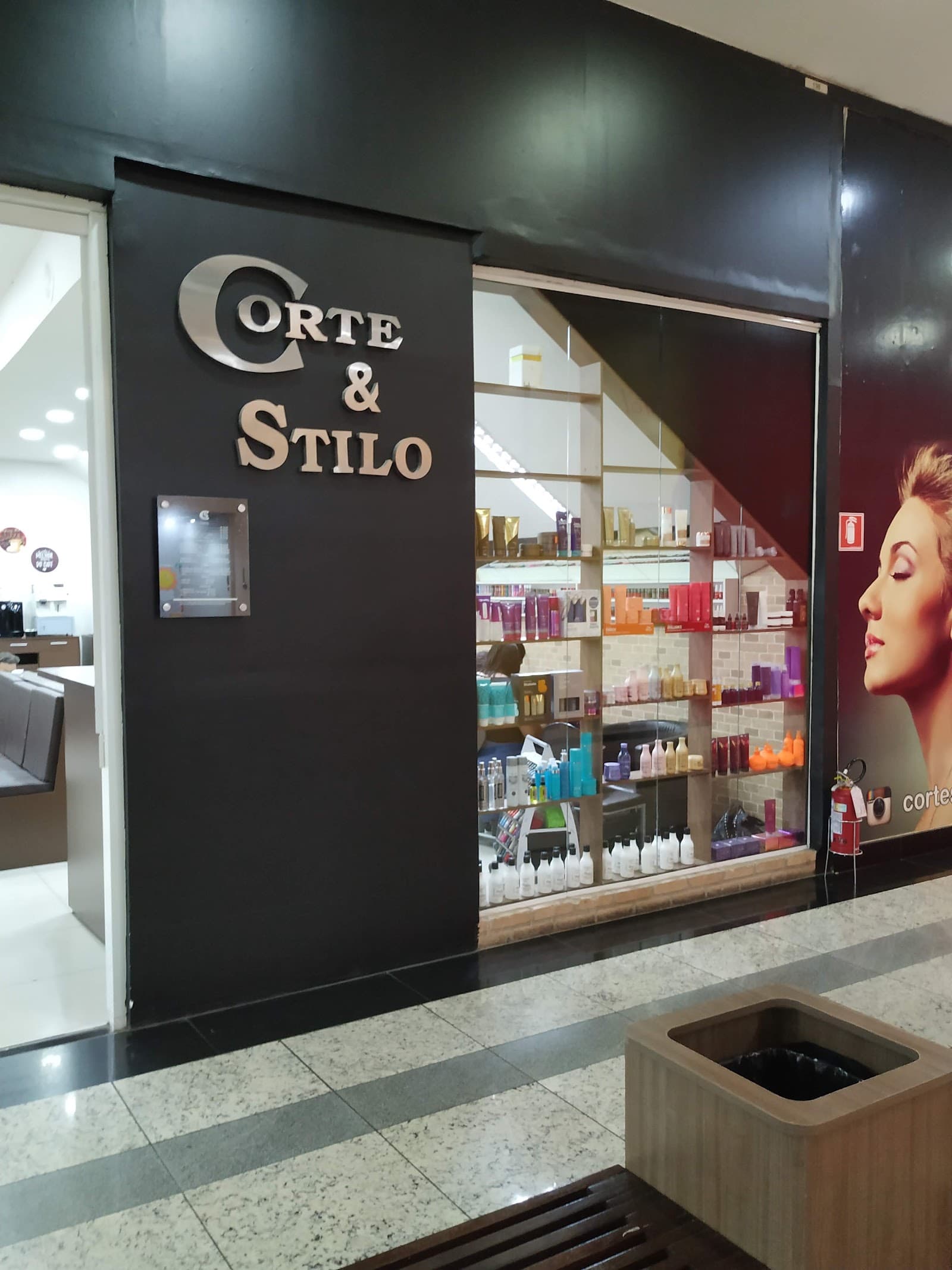 Vitrine da Corte & Stilo no shopping, com o letreiro em metal no painel preto e a estante de produtos