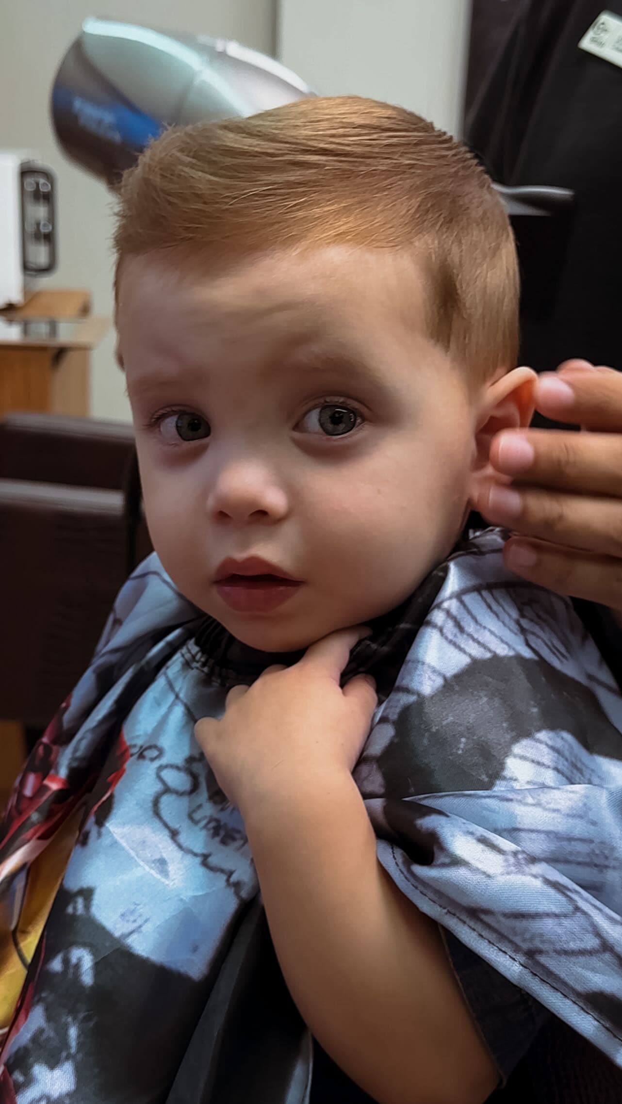 Menino pequeno de capa estampada durante o corte infantil